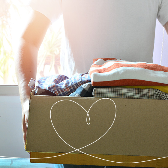 Um homem de camiseta branca, segurando uma caixa de roupas. Por cima da imagem, um desenho de coração.