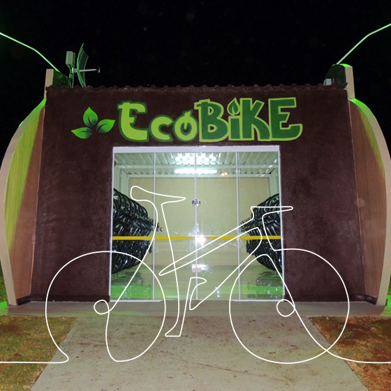 Uma construção de cor cinza e alguns grafites, possui porta de vidro e o nome EcoBike na cor verde. Por cima da imagem, o desenho de uma bicicleta. 